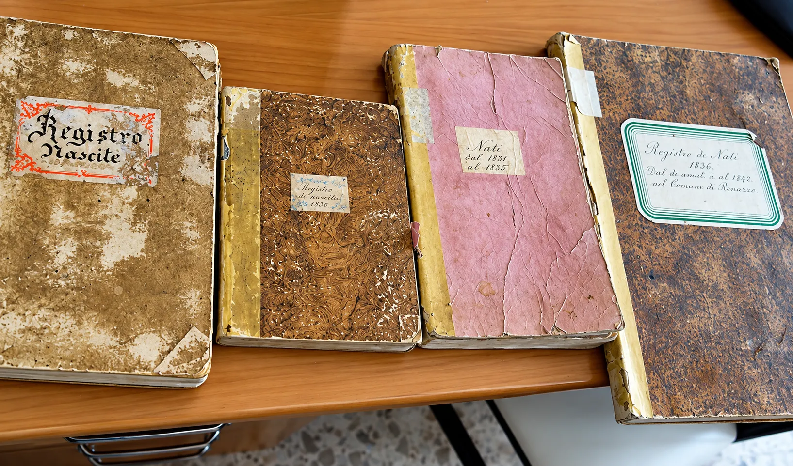 Four old bound civil registers on a desk, one labelled “Registro Nascite”.