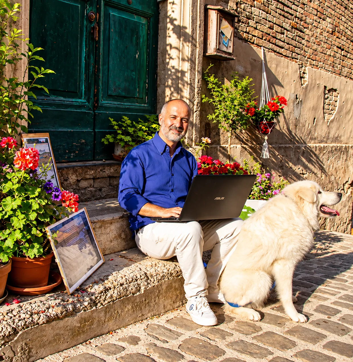 Iuri Silvestri seated on a doorstep with a laptop and a white dog, in a sunlit Italian lane.